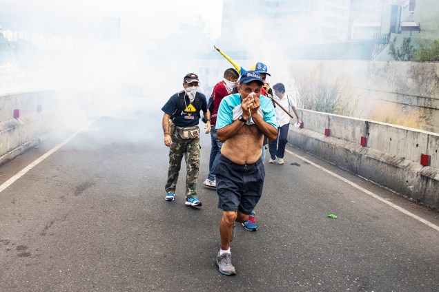 Manifestantes se protegem de bombas de gás lacrimogêneo lançadas pela polícia, durante marcha contra o presidente venezuelano Nicolás Maduro - 23/01/2019