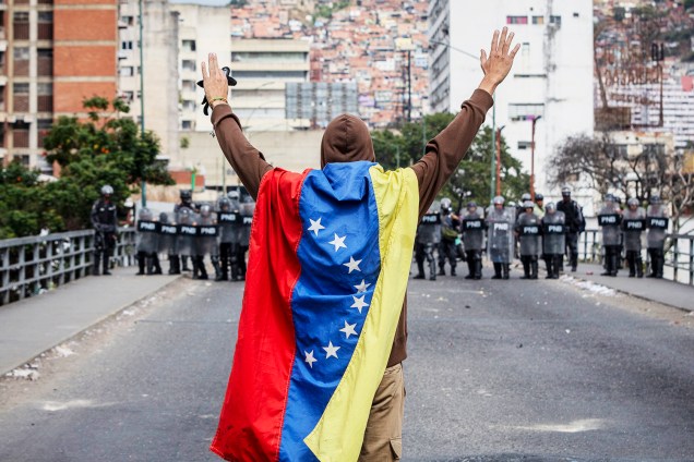 Homem com bandeira da Venezuela levanta os braços na frente de policiais durante marcha contra o presidente Nicolás Maduro - 23/01/2019