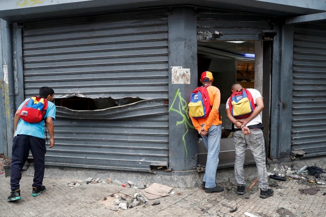 Homens olham dentro de uma loja de liquor saqueada após os protestos contra o governo de Nicolas Maduro em Caracas, na Venezuela - 24/01/2019