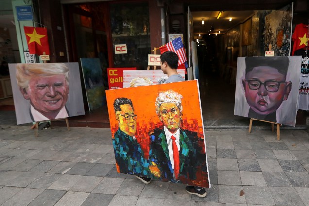Um homem que carrega uma pintura de Donald Trump e Kim Jong-un passa em frente a outras duas pinturas dos líderes de EUA e Coréia do Norte, antes da cúpula que acontecerá em Hanói, no Vietnã - 27/02/2019