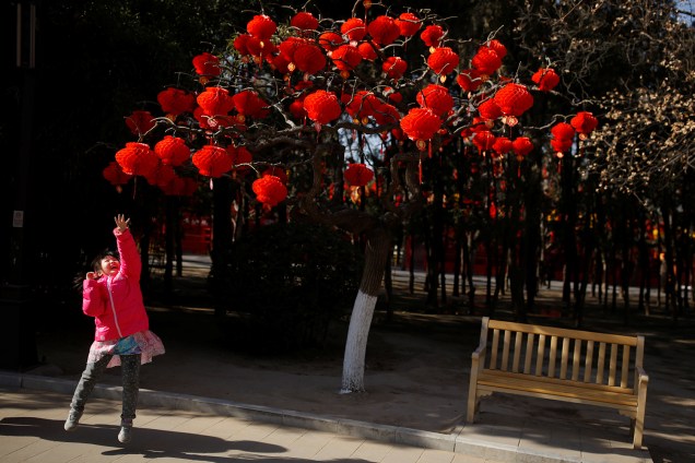 Menina pula para tentar alcançar lanternas vermelhas em árvore no Parque Ditan, Pequim, China - 01/02/2019