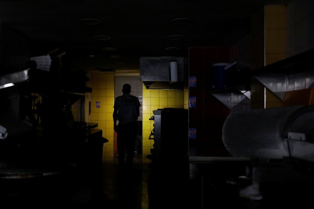 Homem usa o celular para iluminar a cozinha de um restaurante durante blecaute em Caracas, na Venezuela - 07/03/2019