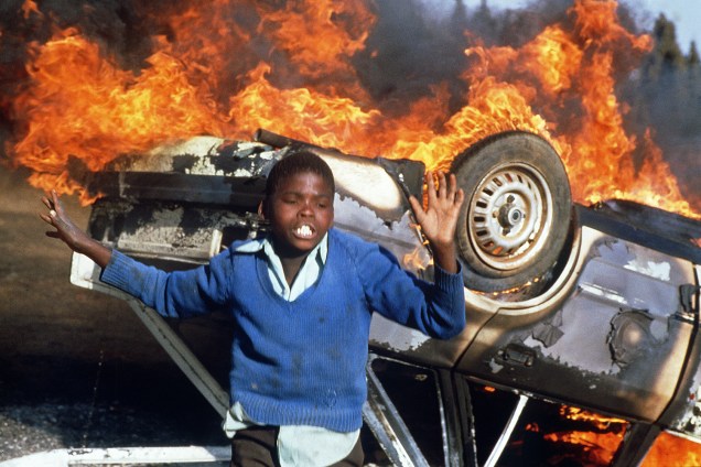 Garoto sul-africano é visto próximo de carro incendiado durante protestos realizados em Duduza, na África do Sul - 10/07/1985