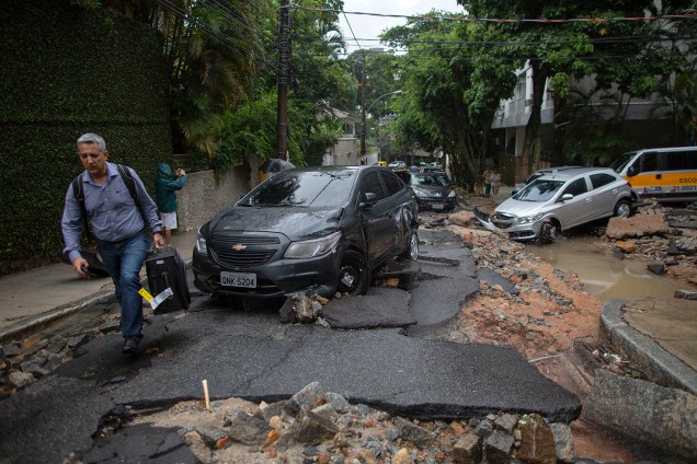 Homem caminha por um rua destruída com carros arrastados pela enxurrada que atingiu o bairro do Jardim Botânico, no Rio de Janeiro - 09/04/2019