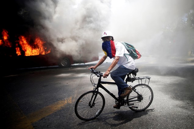 Manifestante da oposição pedala bicicleta próximo de ônibus incendiado, nos arredores da base aérea Generalisimo Francisco de Miranda "La Carlota", em Caracas, capital da Venezuela - 30/04/2019