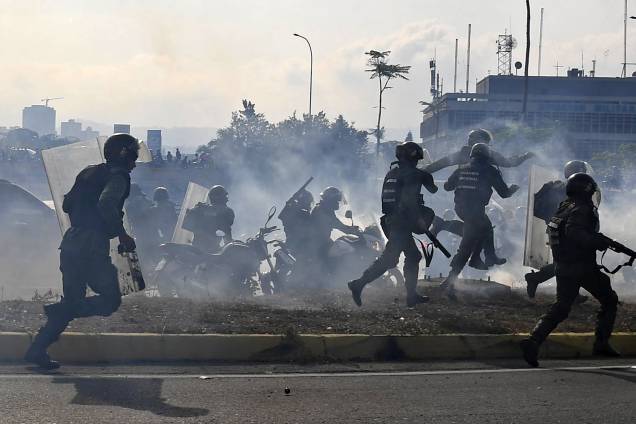 Membros da Guarda Nacional Bolivariana, leais ao presidente Nicolás Maduro, correm sob uma nuvem de gás lacrimogêneo durante confronto com apoiadores de Juan Guaidó em frente à base militar de La Carlota, em Caracas - 30/04/2019
