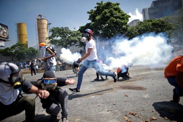 Manifestantes de oposição se protegem de gás lacrimogêneo em uma rua perto da Base Aérea Generalíssimo Francisco de Miranda La Carlota em Caracas durante confronto com forças leais ao presidente Nicolás Maduro - 30/04/2019