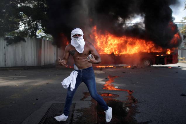 Manifestante de oposição é visto com pedras na frente de ônibus incendiado, próximo da base aérea Generalisimo Francisco de Miranda  "La Carlota"em Caracas, capital da Venezuela - 30/04/2019