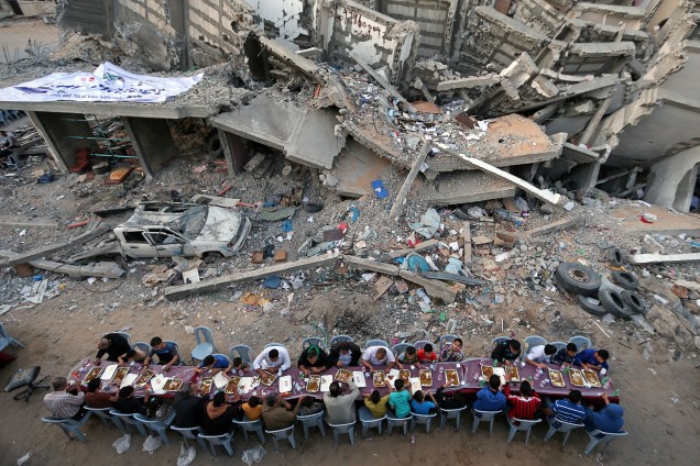 Palestinos quebram jejum comendo as refeições perto dos escombros de um edifício recentemente destruído por ataques aéreos israelenses, na Cidade de Gaza - 18/05/2019
