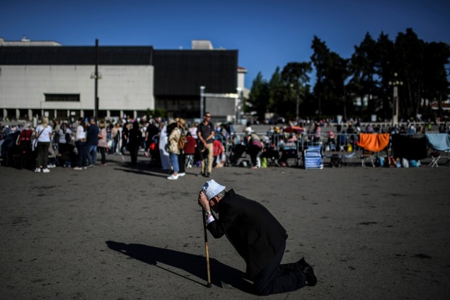 Homem se ajoelha para rezar diante do Santuário de Fátima durante as celebrações da padroeira de Portugal