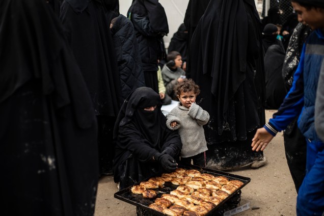 Mulher e criança aguardam a vez para comerem pão no no campo de Al-Hol, que abriga membros do autoproclamado Estado Islâmico (ISIS), no nordeste da Síria