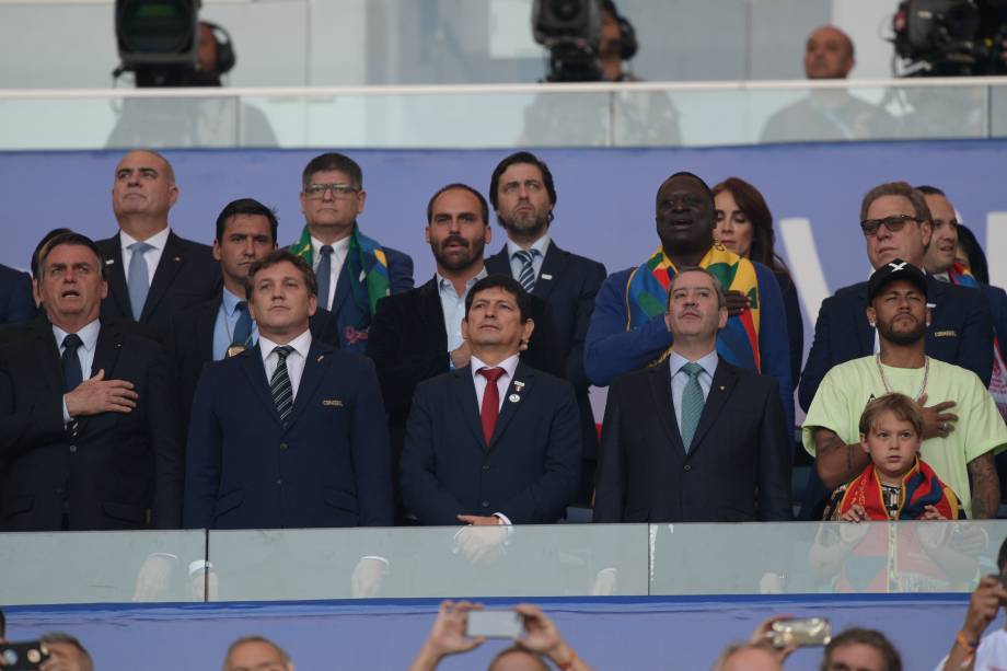 O presidente Jair Bolsonaro (o primeiro da esq. para dir.) e Neymar (o último) põem a mão no peito durante a execução do hino nacional brasileiro no estádio do Maracanã