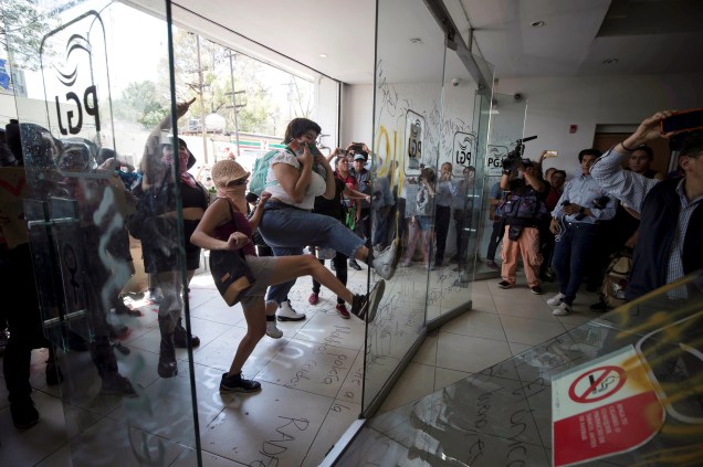 Mulheres manifestantes chutam a porta de vidro da entrada do escritório da Procuradoria Geral da Cidade do México, o protesto foi para exigir justiça depois que a mídia local informou que uma adolescente teria sido estuprada por quatro policiais, no México.