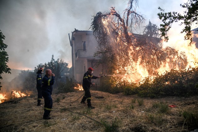 Bombeiros tentam controlar um incêndio perto de uma casa, enquanto um incêndio florestal se acende na aldeia de Kontodespoti, na ilha de Evia, na Grécia