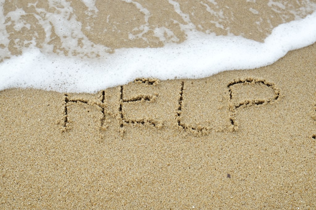 The word HELP written on sand being washed away by wave