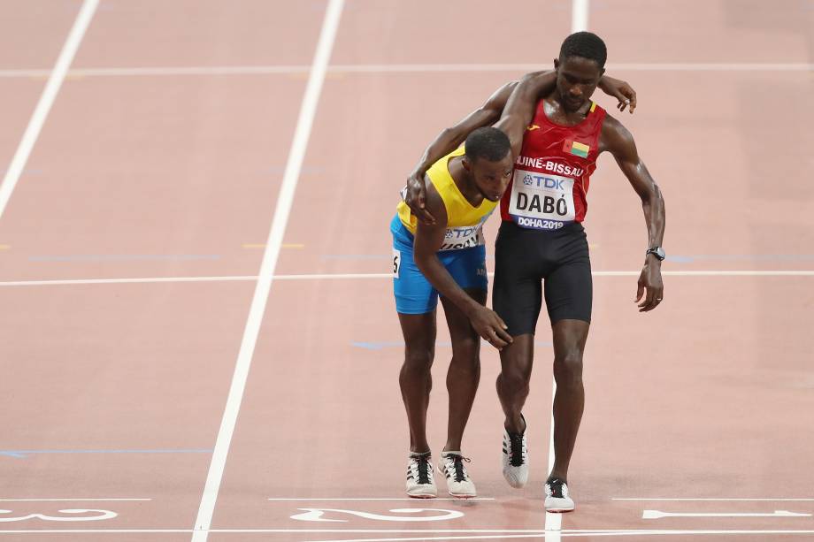 Braima Suncar Dabo, da Guiné-Bissau, ajuda Jonathan Busby de Aruba na linha de chegada nas mangas de 5000 metros masculinos, em Doha, no Catar