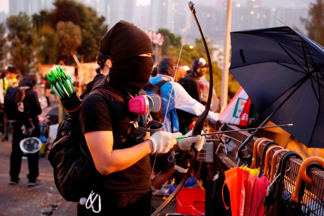 Um manifestante antigoverno utiliza um arco e flecha improvisado durante um impasse com a polícia de choque na Universidade Chinesa de Hong Kong, em Hong Kong, na China