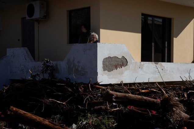 Moradores sentam-se na varanda, enquanto os detritos são recolhidos do lado de fora de suas casas após inundações na cidade de Kineta, Grécia — 25/11/2019