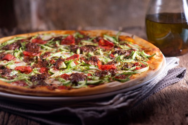 Pizza tocha de fogo: linguiça apimentada, lâminas de abobrinha, mussarela de búfala, molho de tomate e pesto de azeitona preta com uva passa.