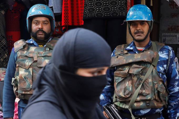 A veiled Muslim woman walks past riot police in a street in Meerut