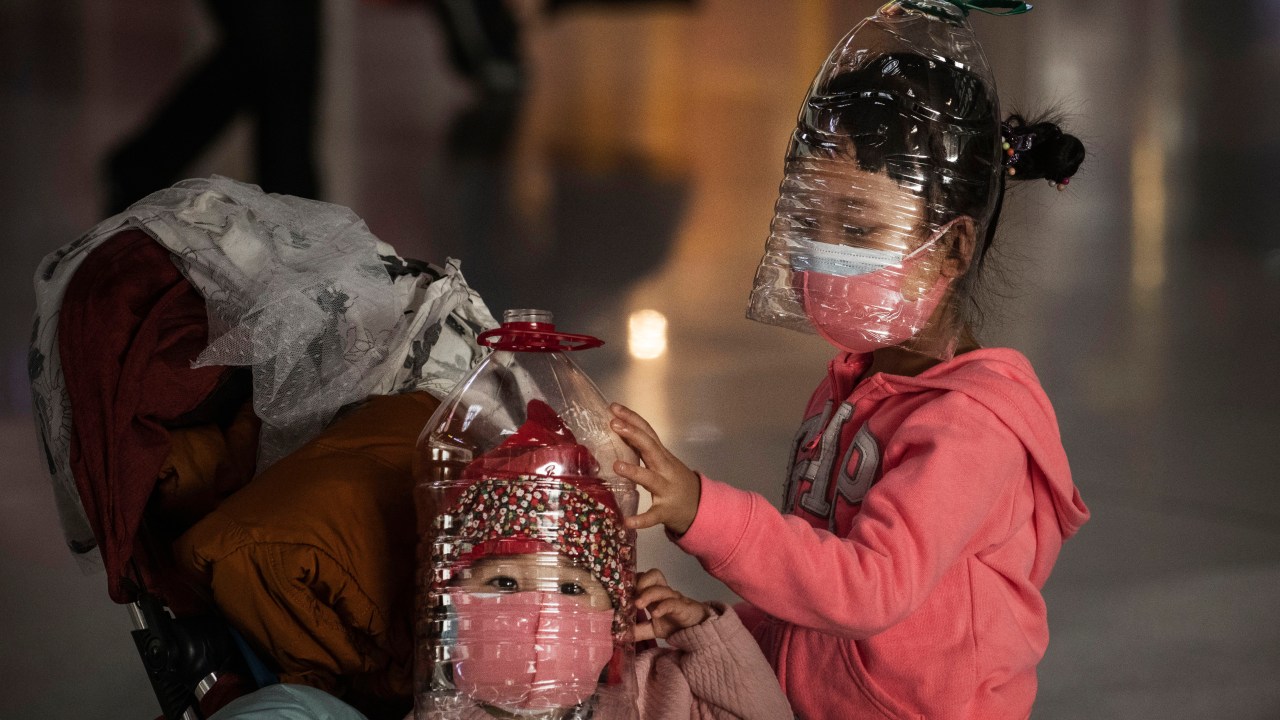 Crianças se protegem do coronavírus com garrafas de plástico e máscara em aeroporto de Pequim (30/01/2020)