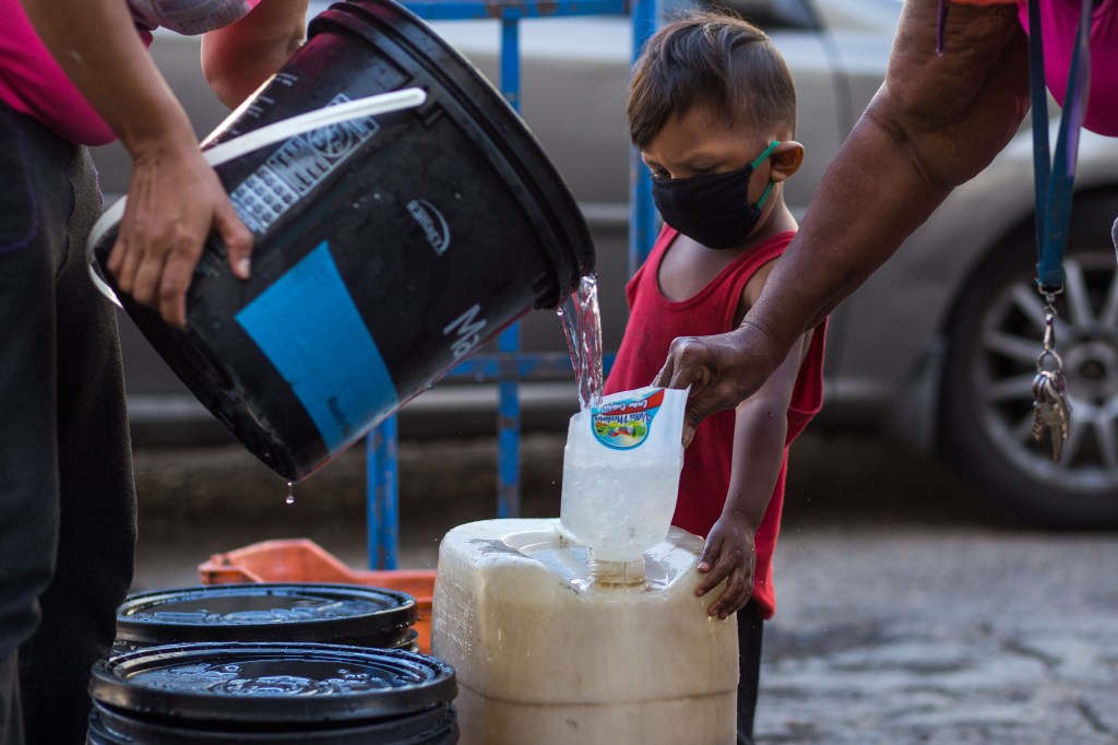Criança com máscara observa coleta de água em recipientes precários em Caracas: crise humanitária e festas nababescas -27/03/2020