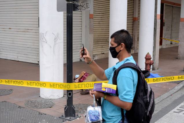 Um homem oferece máscaras à venda perto do corpo de um homem que desabou na calçada, durante o surto de coronavírus