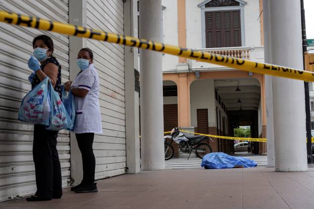 Mulheres próximas ao cadáver de um homem que desmaiou na calçada, durante o surto de coronavírus (COVID-19), em Guayaquil, no Equador