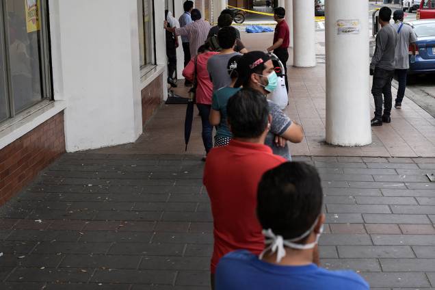 Pessoas ficam na fila em frente a uma loja perto do cadáver de um homem que desmaiou na calçada, durante o surto de coronavírus