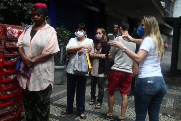 Uma funcionária do banco pede que os clientes mantenham distância enquanto se alinham para entrar no banco durante o surto do coronavírus, no bairro de Copacabana, no Rio de Janeiro