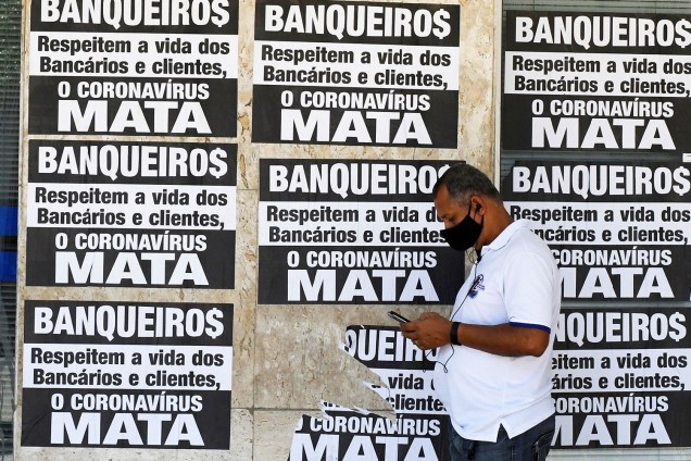 Homem com máscara espera na fila em frente ao banco da Caixa para tentar receber ajuda emergencial do governo federal em meio ao surto do coronavírus, no Rio de Janeiro