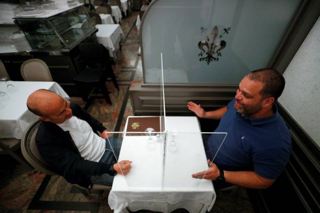 Alberto Iannelli e Fabio Andreotti, proprietários do restaurante Nuova Fiorentina, em Roma, na Itália, testam a tela protetora instalada em uma mesa do restaurante.