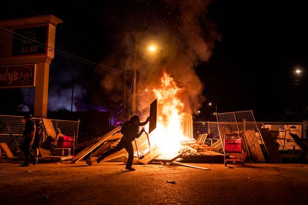Um manifestante lança um pedaço de madeira em um incêndio na rua ao norte da 3ª Delegacia de Polícia em Minneapolis, Minnesota