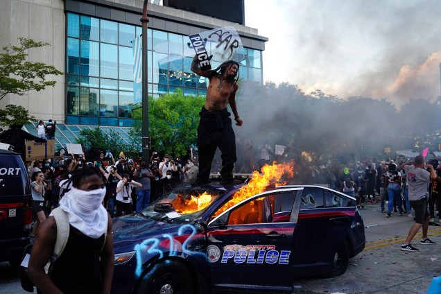 Um manifestante sobe em cima de um carro da polícia em chamas durante um protesto em Atlanta, Geórgia - 29/05/2020