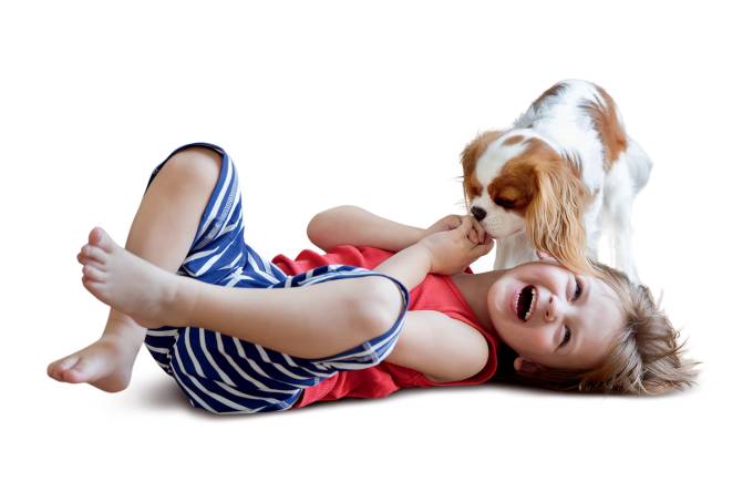 Little boy lying on the floor in the living room laughing because his dog licking his hand