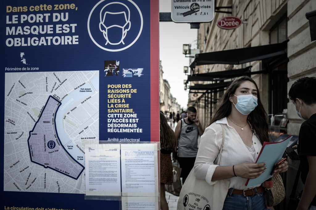 Mulher vista com máscara ao lado de placa que indica obrigatoriedade de proteção facial, em Bordeaux, França. 16/09/2020