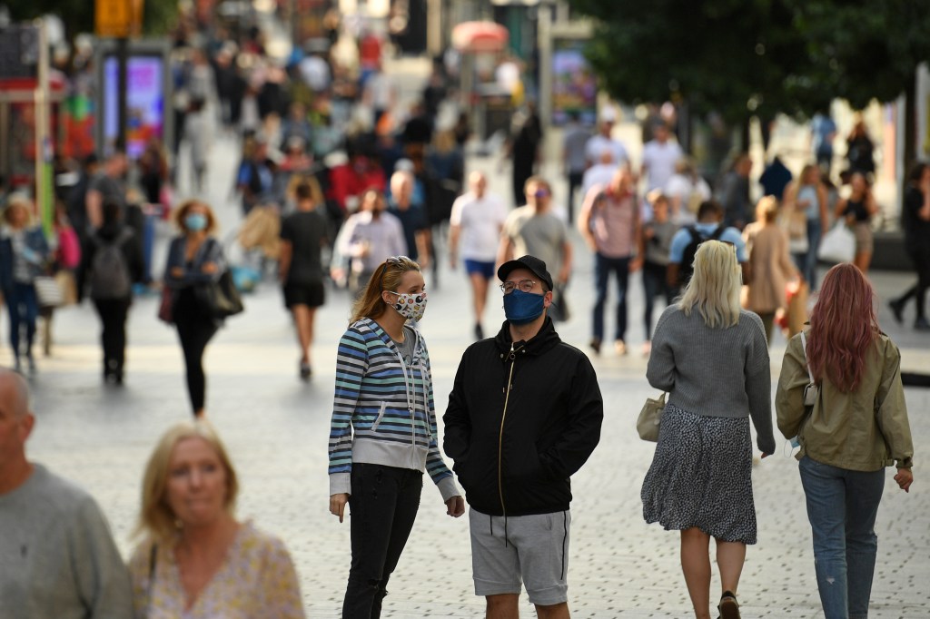 Casal com máscaras conversa em rua movimentada no centro de Liverpool, na Inglaterra.