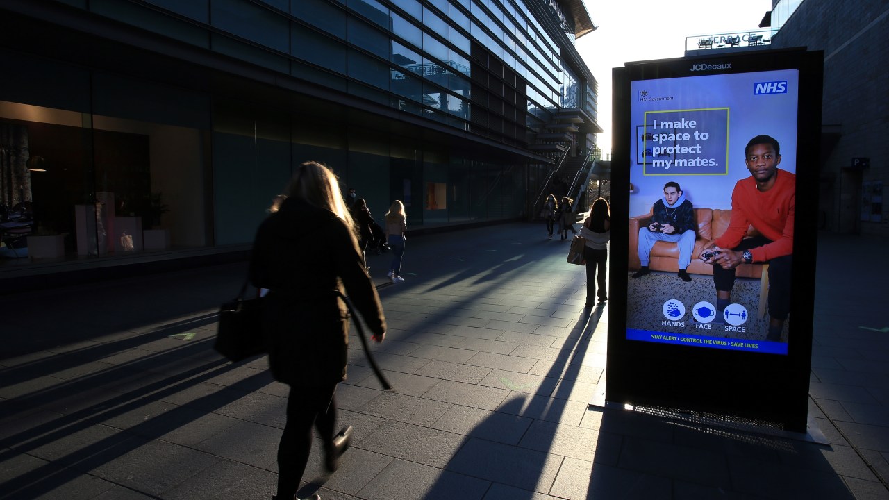 Mulher passa por uma placa digital informando os pedestres sobre as últimas orientações do governo sobre o coronavírus, em Liverpool, noroeste da Inglaterra - 01/10/2020