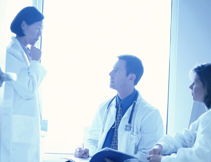 três médicos discutindo. dois estão sentados e uma médica em pé