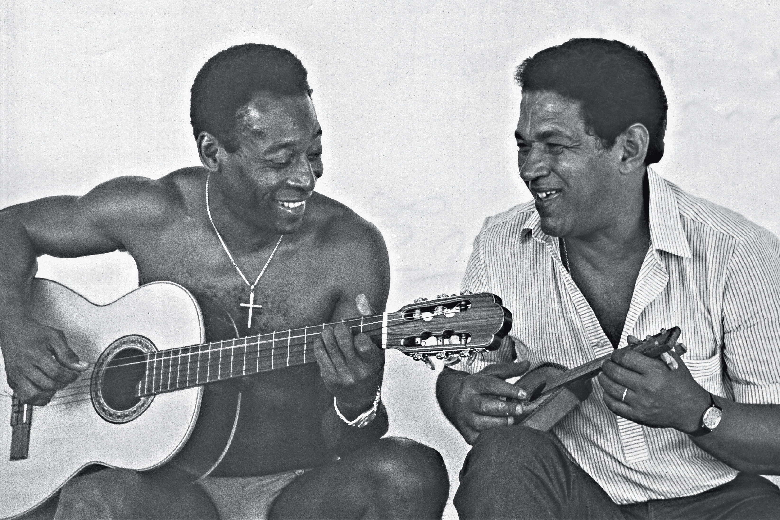 Pelé tocando violão e Garrincha tocando um violão bem pequeno, de brinquedo.