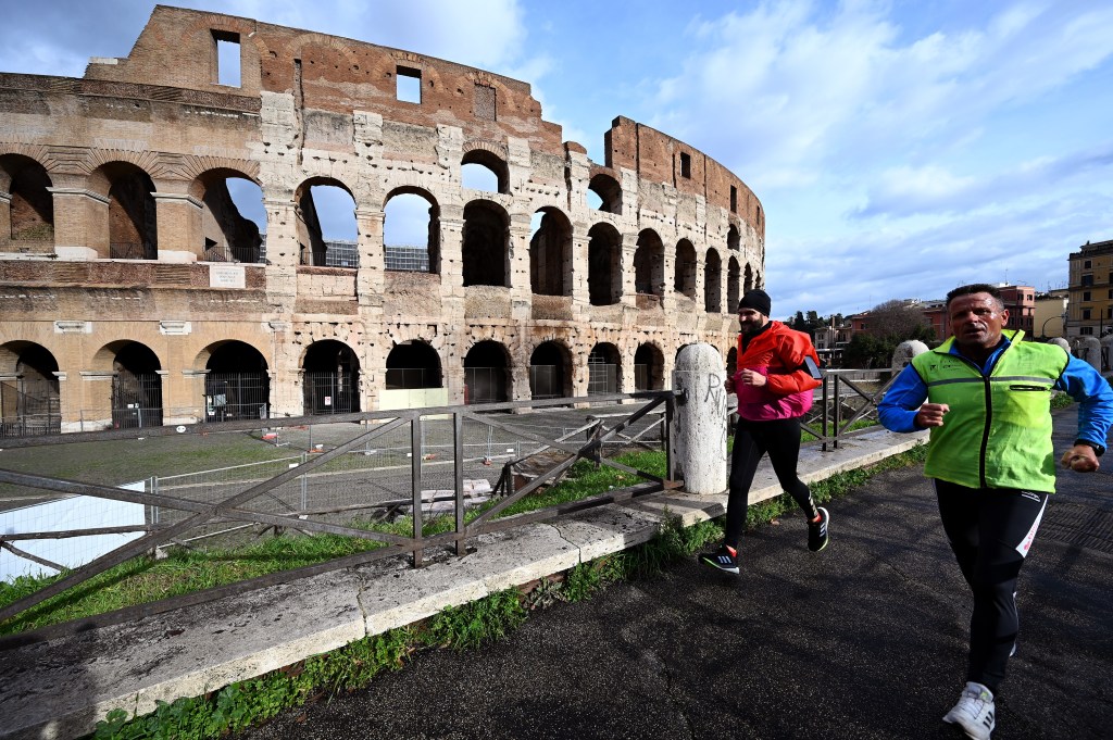 Men run by the Colisseum in an empty Rome