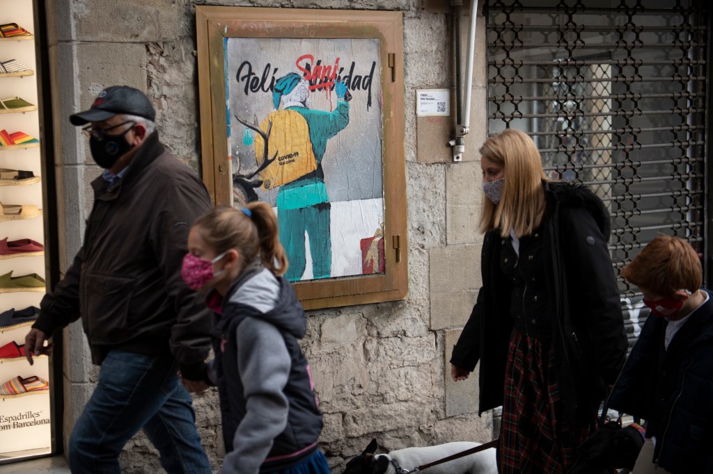 Grupo de pessoas em Barcelona, Espanha, passa por obra do artista de rua italiano TvBoy que mostra o Papai Noel carregando a vacina contra a Covid-19. 24/12/2020