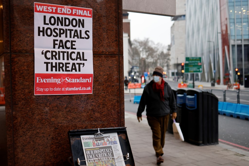A pedestrian wearing a facemask walks past a stand with the Evening Standard newspapers in central London on January 8, 2021, as England entered a third lockdown due to the novel coronavirus Covid-19. - Faced by a sharp rise in coronavirus infections, driven by the new strain, England entered a strict lockdown on January 5, 2021, with schools and non-essential shops closed for at least six weeks after previous measures failed to halt the steep rise in cases. (Photo by Tolga Akmen / AFP)