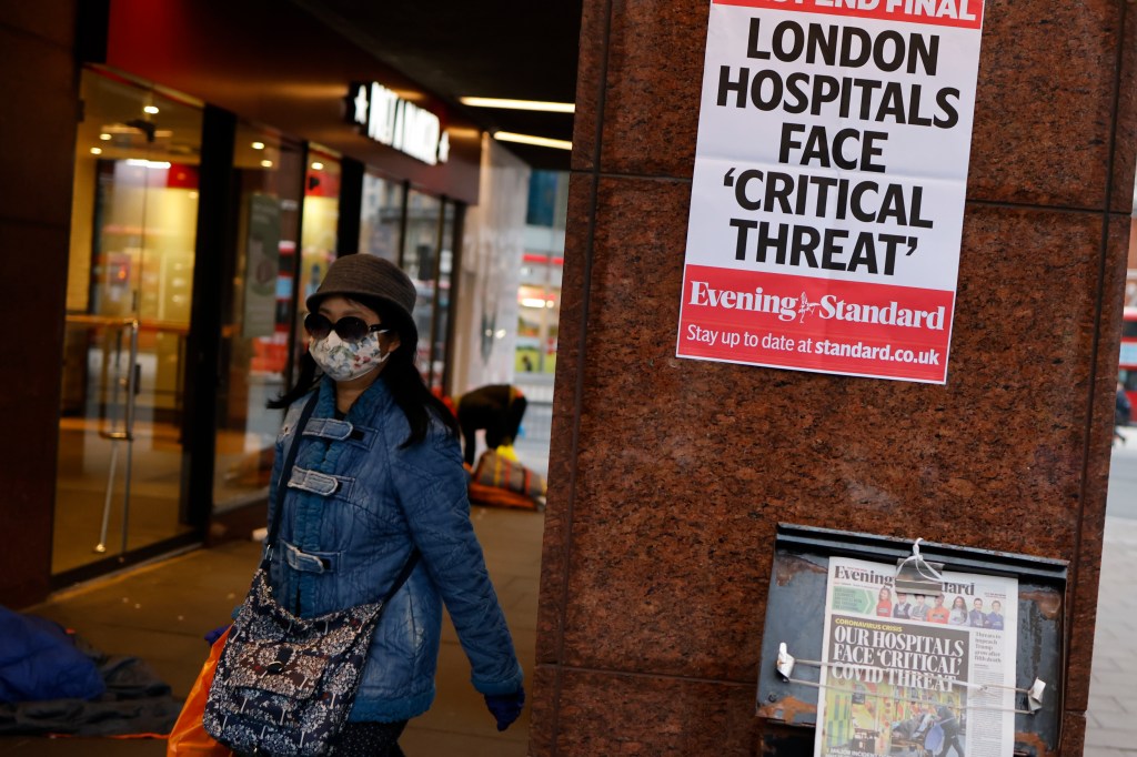 Mulher de máscara ao lado de estande do jornal Evening Standard, no qual se lê "Hospitais de Londres enfrentam 'ameaça crítica'". 08/01/2021