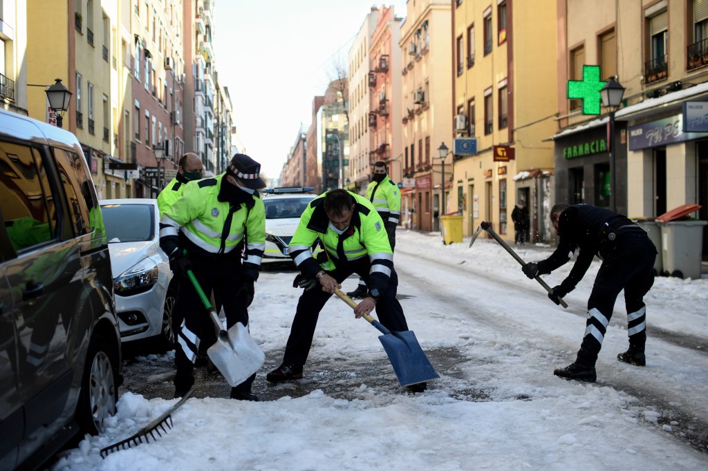 Os guardas de trânsito locais limpam a neve congelada da calçada em Madri em 12 de janeiro de 2021.