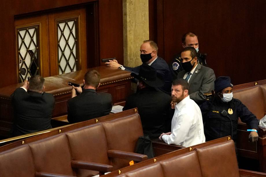 Policiais do Capitólio dos EUA apontam suas armas para uma porta que foi vandalizada na Câmara durante uma sessão conjunta do Congresso -