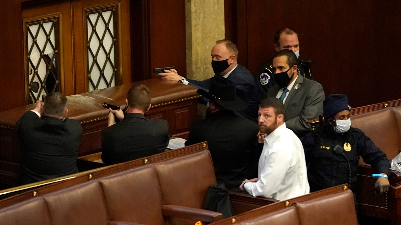 Policiais do Capitólio dos EUA apontam suas armas para uma porta que foi vandalizada na Câmara durante uma sessão conjunta do Congresso - 06/01/2021