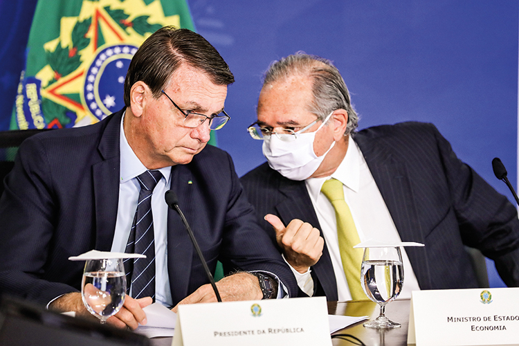 URGÊNCIA - Bolsonaro e Paulo Guedes: reformas fundamentais para o país também dependem do empenho do presidente - Na imagem Paulo Guedes conversa com o presidente Jair Bolsonaro, apenas Guedes está usando máscara de proteção com COVID-19.