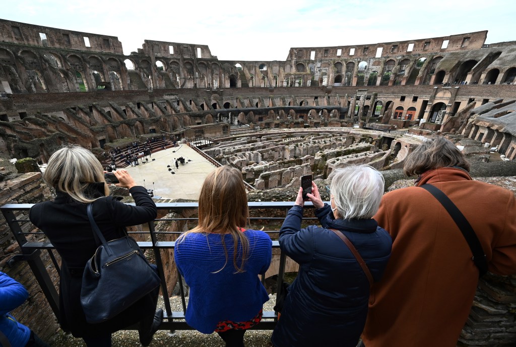 visitors take pictures as singers and musicians from the Santa Cecilia academy perform on February 1, 2021 at Rome's landmark Colosseum as it reopens amid an easing of coronavirus restrictions, with all but five Italian regions put in the low-risk "yellow" category from today. (Photo by Vincenzo PINTO / AFP)