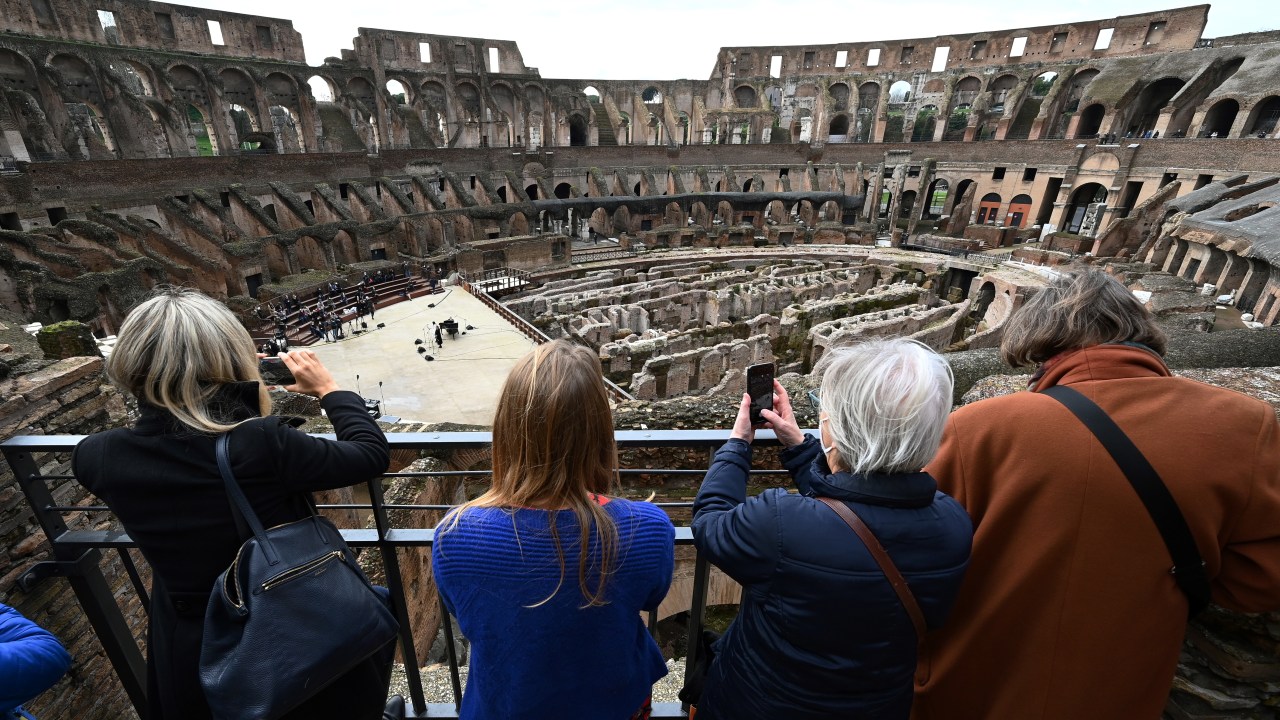 visitors take pictures as singers and musicians from the Santa Cecilia academy perform on February 1, 2021 at Rome's landmark Colosseum as it reopens amid an easing of coronavirus restrictions, with all but five Italian regions put in the low-risk "yellow" category from today. (Photo by Vincenzo PINTO / AFP)